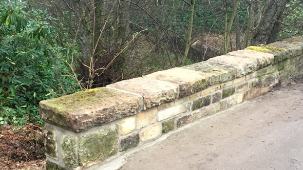 stone bricked garden wall separating woodland from pathway