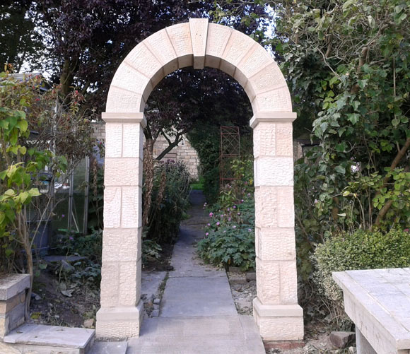 stone archway in garden surrounded by trees with a stone slab path leading away